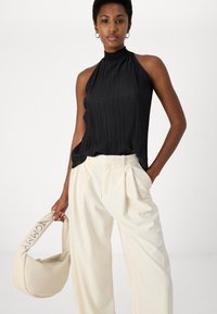 Black pleated halter top with a high neckline, paired with cream wide-leg trousers and a cream handbag featuring a logo.