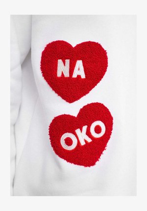 Biela mikina s dvoma červenými srdcovými záplatami s textúrovanými povrchmi, zobrazujúca biele písmená "NA" a "OKO" v každom srdci.