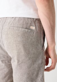 Light brown linen trousers with a textured finish, featuring a rear pocket and a small BOSS label. The silhouette is tailored and fitted.