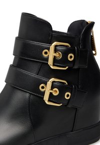 Stivale in pelle nera alla caviglia con due fibbie dorate sulle cinghie e una suola testurizzata. Superficie liscia con un design elegante. Dettaglio con zip laterale.