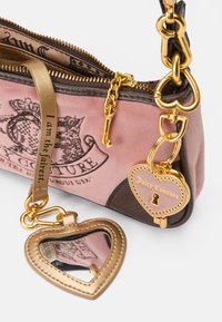 Ροζ σουέτ τσάντα χειρος με σκούρες καφέ λεπτομέρειες, χρυσά αξεσουάρ και ένα χαριτωμένο κρεμαστό καθρεφτάκι σε σχήμα καρδιάς. Διαθέτει λογότυπο τυπωμένο και διακοσμητικό φερμουάρ.