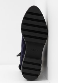 Czarna gumowa podeszwa z poziomymi rowkami i logo DKNY. Cholewka wykonana z granatowego zamszu o fakturowanym wykończeniu z futrzanymi akcentami.