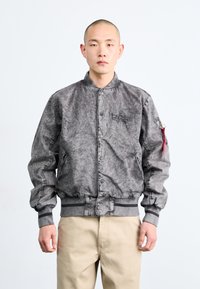 Gray bomber jacket with textured fabric, ribbed cuffs and hem, snap buttons, and a side pocket featuring a red loop detail.