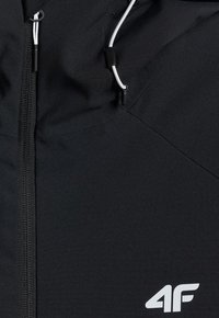 Veste noire à l'avant avec fermeture éclair, cordons blancs réglables à la capuche et logo blanc "4F" en bas à droite.