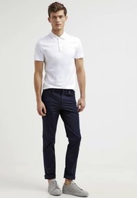 Hvid poloshirt med to-knaps placket, kombineret med marineblå bukser og lysegrå sneakers. Stoffet fremstår glat og tætsiddende.