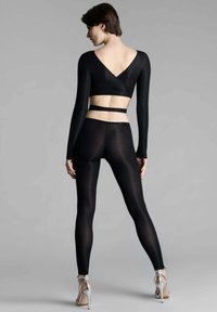 Crop top noir à manches longues avec un dos en forme de V, associé à des leggings noirs ajustés. L'ensemble est composé d'un tissu lisse et extensible, complété par des talons argentés.