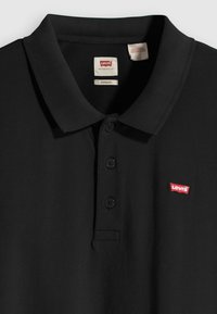Juodas polo marškinėlis iš tekstūruotos medžiagos, su trijų sagų užsegimu ir mažos raudonos Levi's logotipu ant kairiojo krūtinės.