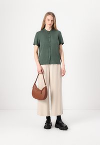 Grønn kortermet skjorte med knapper, beige vide bukser, svarte kraftige sko, og brun lær skulderveske. Glatt tekstur, skreddersydd passform.
