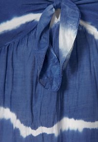 Modrý a bílý tie-dye materiál s uzlovým předním detailem, který se vyznačuje měkkou, lehkou texturou a nařaseným pasem.