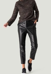 Pantalon noir en simili cuir à taille haute, jambes effilées et poches latérales, associé à un pull texturé foncé et des baskets noires.