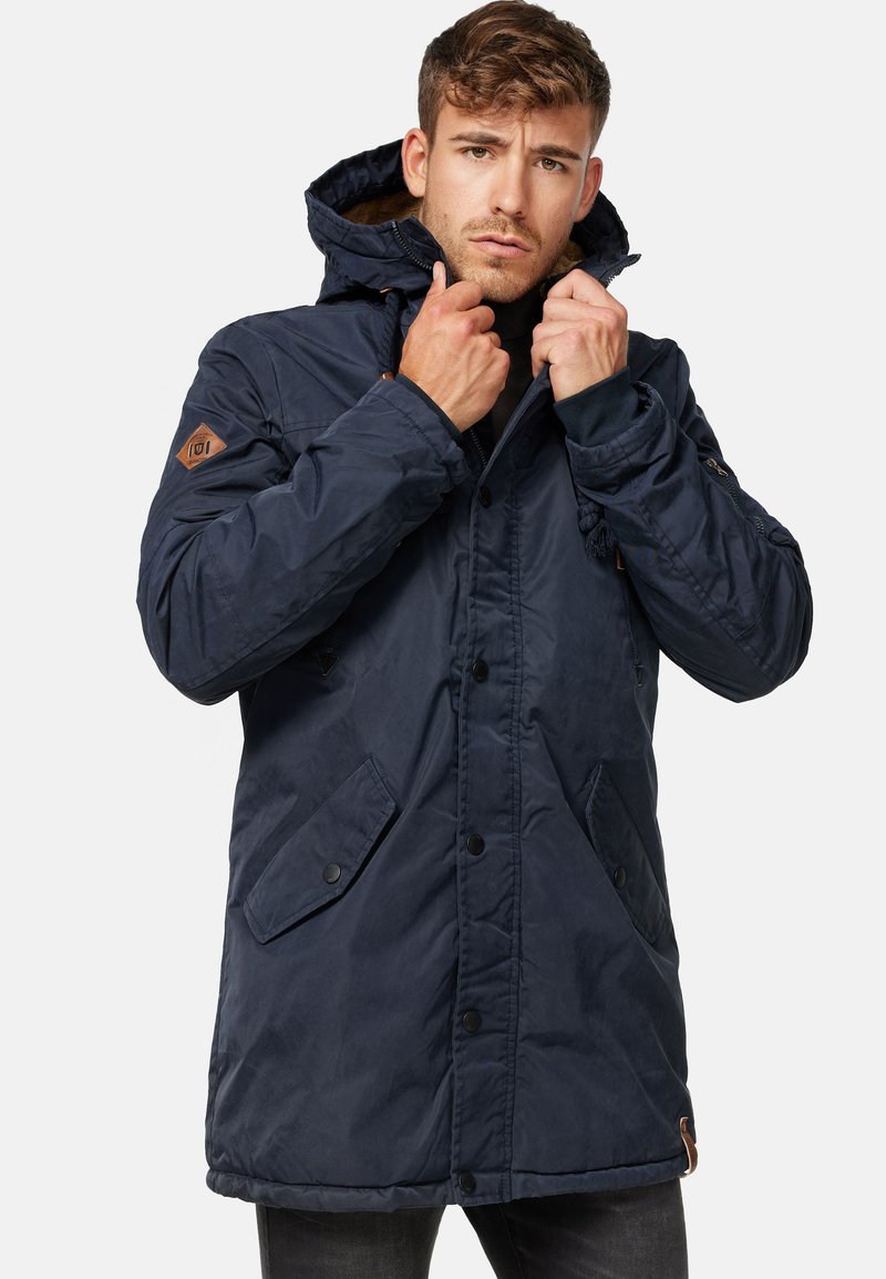 Parka bleu marine avec capuche, présentant un devant zippé, une fermeture à boutons et des poches texturées. Comprend des accents en cuir marron.