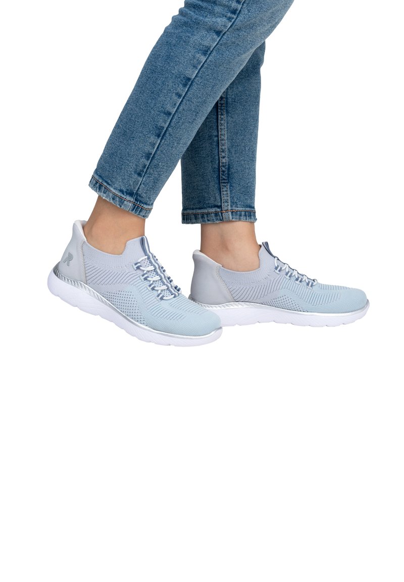 Scarpe da ginnastica a rete di colore azzurro chiaro con un design testurizzato, chiusura con lacci e suola in gomma bianca, visibili contro jeans di denim.