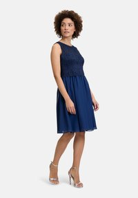 Tengerészkék ruha, csipkés felsőrésszel, ujjatlan kialakítással és lenge chiffon szoknyával, ezüst pántos magassarkúval párosítva.