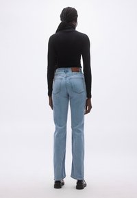 Svijetloplave traperice trapezastog kroja s visokim strukom, pet džepova i smeđom kožnom oznakom straga. Crni top s dugim rukavima.