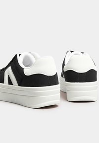 Svartvita sneakers med en texturerad ovandel, vadderad krage och en tjock vit gummisula. Har en minimalistisk design och sidodetaljer.
