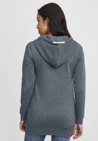 Grå hoodie i mjukt tyg, med dragsko i huvan, långa ärmar och en något böjd nederkant. Läderdetalj på baksidan.