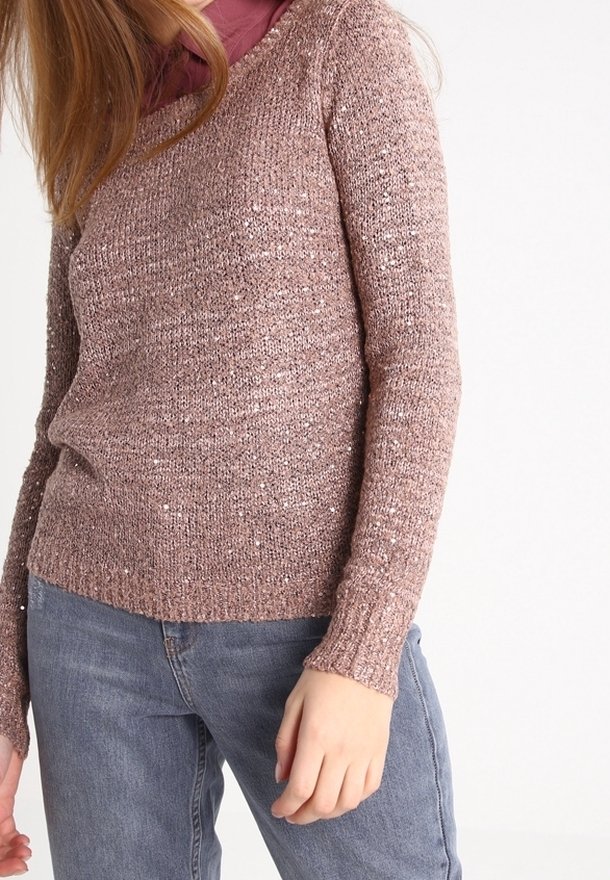 Rosa gestrickter Pullover mit Rundhalsausschnitt und langen Ärmeln, mit einer strukturierten Oberfläche und dezenten metallischen Fäden. Kombiniert mit hellblauen Jeans.