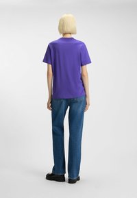 Purple short-sleeve t-shirt, crew neck, smooth texture, paired with wide-leg blue jeans and black chunky shoes. Minimalistic design.