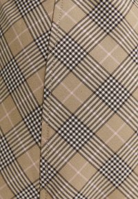 Beige tyg med ett rutmönster som har svarta, vita och rosa inslag. Slät struktur med synlig sömdetalj.