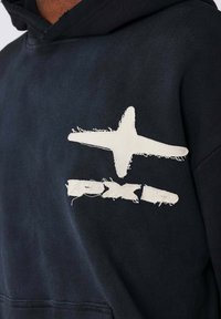 Sudadera negra con un gran gráfico de estrella blanca deshilachada y el texto "PXD". El material parece suave con una textura visible.