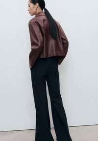 Brown leather cropped jacket with wide sleeves, paired with black flared trousers. Smooth texture, minimal hardware, and fitted silhouette.
