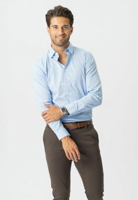 Světle modrá košile na knoflíky s límečkem, dlouh�ými rukávy a slim fit, zkombinovaná s tmavě hnědými kalhotami a stříbrnými hodinkami.
