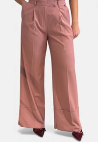 Pantaloni a gamba larga in tessuto color rosa tenue, con vita alta, pieghe e orli risvoltati. Abbinati a décolleté appuntite color bordeaux.