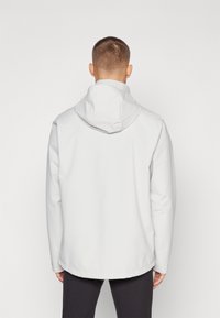 Chaqueta con capucha de color gris claro y acabado mate liso. Presenta un corte recto y puños elásticos. Diseño minimalista sin hardware visible.