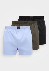 Trois paires de boxers pour homme en bleu clair, vert olive et noir, disposées en chevauchement sur un fond blanc.