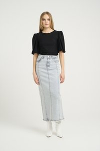 Svart kortermet topp med puffærmer, kombinert med et lyseblått denimskjørt. Modellen har på seg hvite spisse ankelstøvler. Enkel, minimalistisk design.
