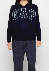 Mörkblå huvtröja i mjukt tyg med en stor ljusblå "GAP" logga fram och ribbade ärmslut och nederkant.