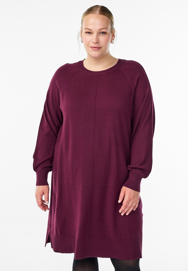 Haljina do koljena tamnocrvene boje s dugim rukavima, okruglim izrezom i bočnim prorezima; izrađena od mekog, teksturiranog pletenog materijala.