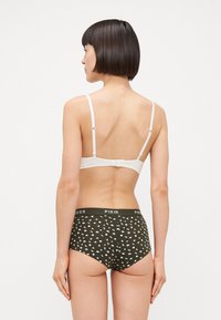 Bralette branca com alças ajustáveis, combinado com cuecas de cintura alta verde-escuro com padrão floral branco e cintura com logótipo.