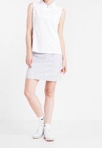 Bílý bezrukávový polo s límečkem na zip, doplněný světle šedou sukní s jemným květinovým vzorem. Bílé sportovní boty.