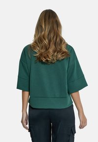 Zelená zkrácená mikina s volným střihem, širokými rukávy a hladkým povrchem. Nosit s tmavými cargo kalhotami; jednoduchý design bez viditelných log. 