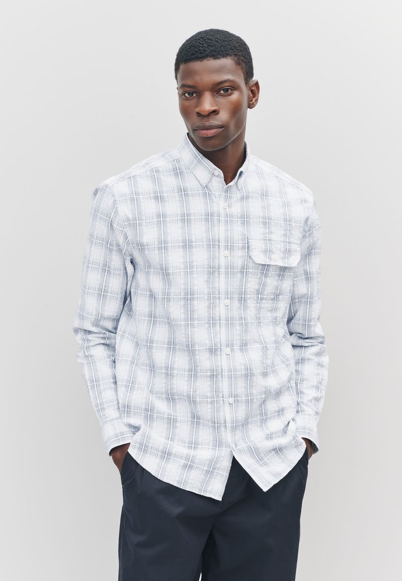 Camicia a quadri azzurro chiaro e bianca con bottoni, realizzata in tessuto dalla texture morbida. Presenta una tasca sul petto e un colletto standard.