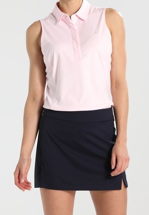 Donna che indossa una camicia senza maniche rosa chiaro con colletto e una gonna blu navy al ginocchio con una piccola spacco laterale.