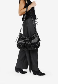 Bolso de mano de cuero negro con un diseño recogido, tachuelas plateadas y un acento de hebilla. Presenta una correa de hombro desmontable y un acabado texturizado.