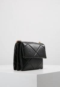 Borsa a tracolla in pelle nera trapuntata con una catenella dorata, caratterizzata da una chiusura a patta e una forma rettangolare strutturata. Superficie testurizzata con motivo a diamante.