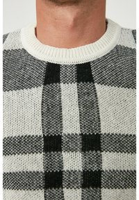 Suéter de punto con un patrón de cuadros en blanco y negro, cuello redondo acanalado y tejido texturizado para brindar calidez y comodidad.