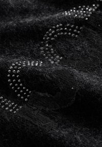 Zwarte wolstof met een patroon van kleine, glanzende zilveren studs. De textuur lijkt zacht en pluizig met zichtbare pluisjes.