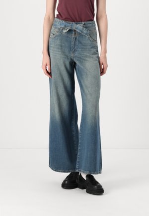 Lyseblå vide jeans laget av denim, med belte i midjen, frontlommer, og en gradvis falming i fargen fra topp til bunn.