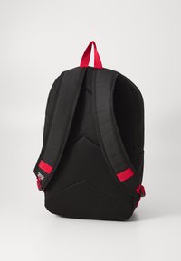 Zwarte rugzak met een gevoerde mesh achterkant, twee verstelbare schouderbanden, een rode handgreep, rode strapdetails en een klein logo op één strap.