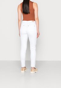 Witte skinny jeans met een gladde textuur en een fitted ontwerp. De achterkant toont twee achterzakken en een merklabel op de tailleband.