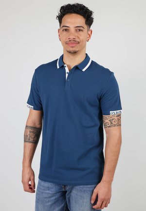 Polo shirt marine en coton, avec un col blanc et des finitions blanches aux manches, et un accent logo sur la manche gauche. Coupe classique.
