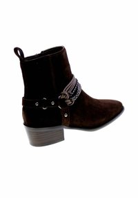 Stivale alla caviglia in suede marrone con tacco a blocco. Caratterizzato da cinturini intrecciati e dettagli metallici. Chiusura con zip laterale per un facile accesso.