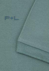 Sweter dziergany z miękkiego materiału w odcieniu teal, z prążkowanymi mankietami i teksturowanym ciałem. Haftowane logo z przodu.