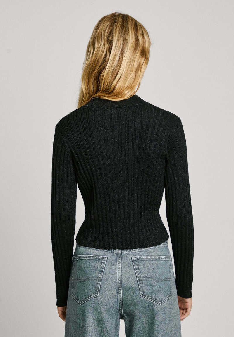 Maglione nero a coste con maniche lunghe, vita aderente e scollatura rotonda. Indossato con jeans chiari a vita alta, che mettono in mostra i dettagli posteriori.