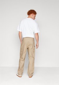 Beige cargo bukser med flere sidelommer, parret med en løstsiddende hvid t-shirt. Stoffet ser holdbart og letvægts ud.