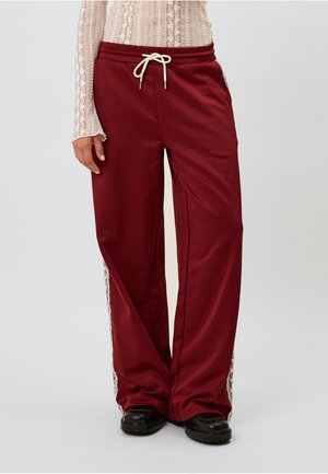 Maroon sweatpants with a relaxed fit, drawstring waistband, and white decorative side stripes. Made of soft, smooth fabric with a slight sheen.